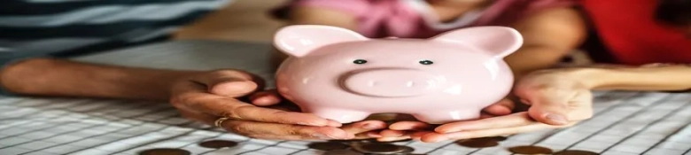 Four hands holding a pink piggy bank over a pile of coins, symbolizing savings or financial planning.