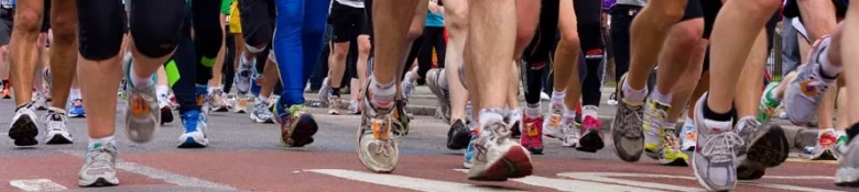 Close-up of runners' legs and feet during a marathon, showcasing a variety of athletic shoes and dynamic movement.