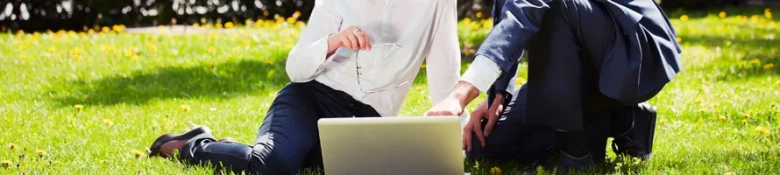 Two people sitting on grass pointing at a laptop