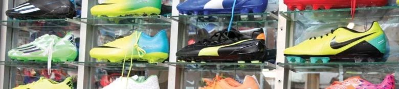 Variety of colorful soccer cleats displayed on glass shelves in a retail store.
