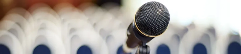 Close-up of a microphone with blurred audience in the background at a conference event.