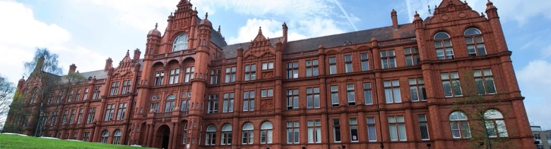 The Peel Building at the University of Salford, showcasing its red brick architecture and large windows under a blue sky.