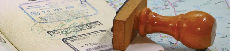 Close-up of a passport with entry stamps and a wooden immigration stamp on a map, symbolizing international travel.