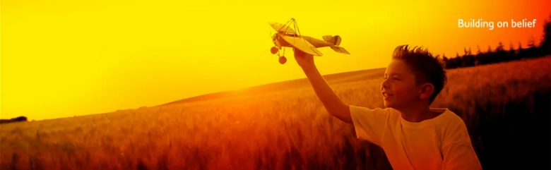 The words "building on belief" in the corner of a sunset background with young boy playing with a toy airplane