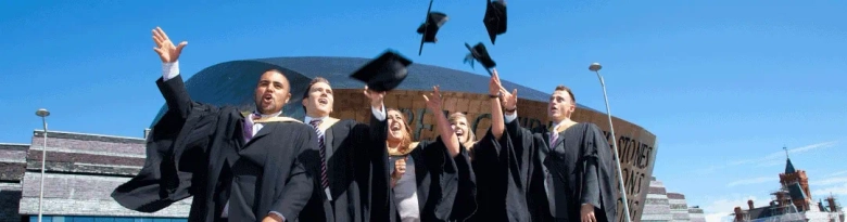 Group of graduates throwing their caps in the air in celebration outside Cardiff Metropolitan University.