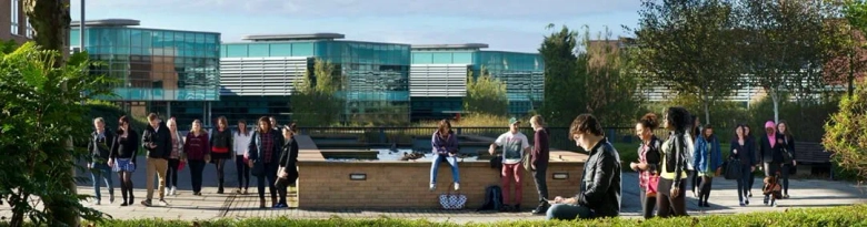 Students walking and socializing on the campus of Edge Hill University with modern buildings in the background.