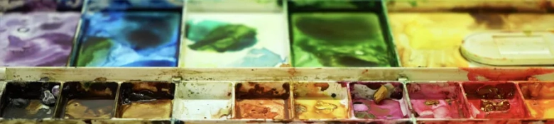 Close-up of a well-used watercolor paint palette with a variety of vibrant colors.