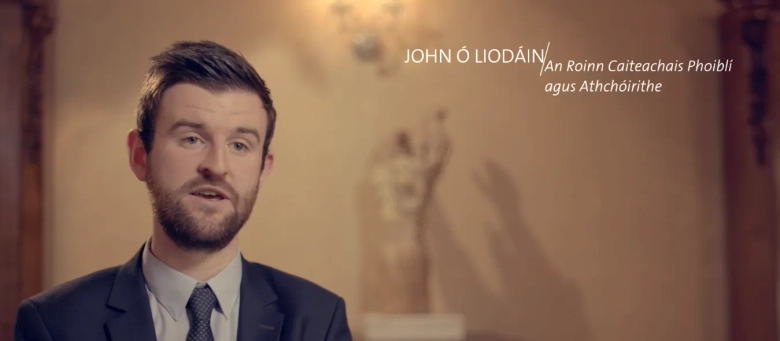 John Ó Liodáin, an administrative officer, speaking with his name and title displayed in text overlay.