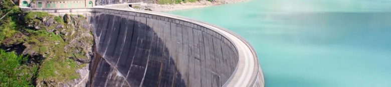 Curved dam wall holding back turquoise water with a road running along the top.