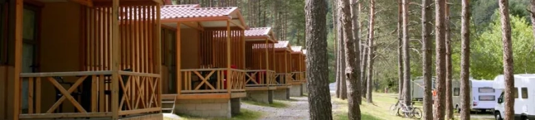 Row of wooden cabins in a forested area with a recreational vehicle parked nearby