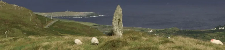 Sheep grazing on a hill with an ancient standing stone overlooking the sea, symbolizing natural and historical environmental conservation.
