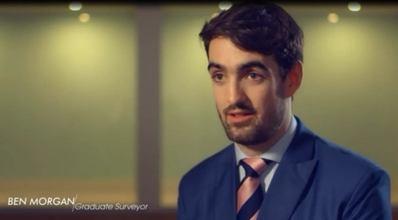 Graduate surveyor Ben Morgan in a blue suit and pink tie speaking during an interview.