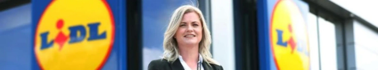 image of a blonde woman in a suit standing in front of a lidl store