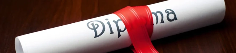 Close-up of a rolled diploma with a red ribbon on a wooden surface.